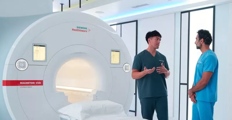 Two clinicians talking beside a Siemens MRI scanner in a modern imaging suite.