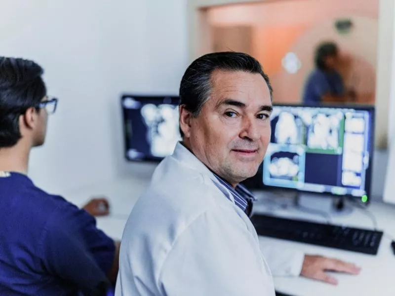 Radiologist reviewing medical scans on a computer workstation while a colleague works beside them.