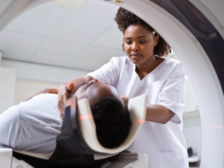 Radiographer positioning a patient’s head inside an MRI scanner before imaging.