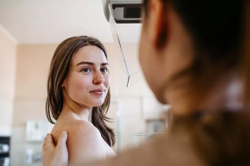 Woman undergoing a breast imaging exam, standing still while a clinician positions the scanner.