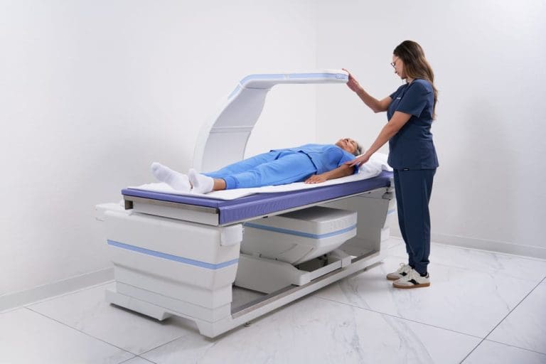 Clinician positioning an overhead imaging arm above a patient lying on a medical examination table.