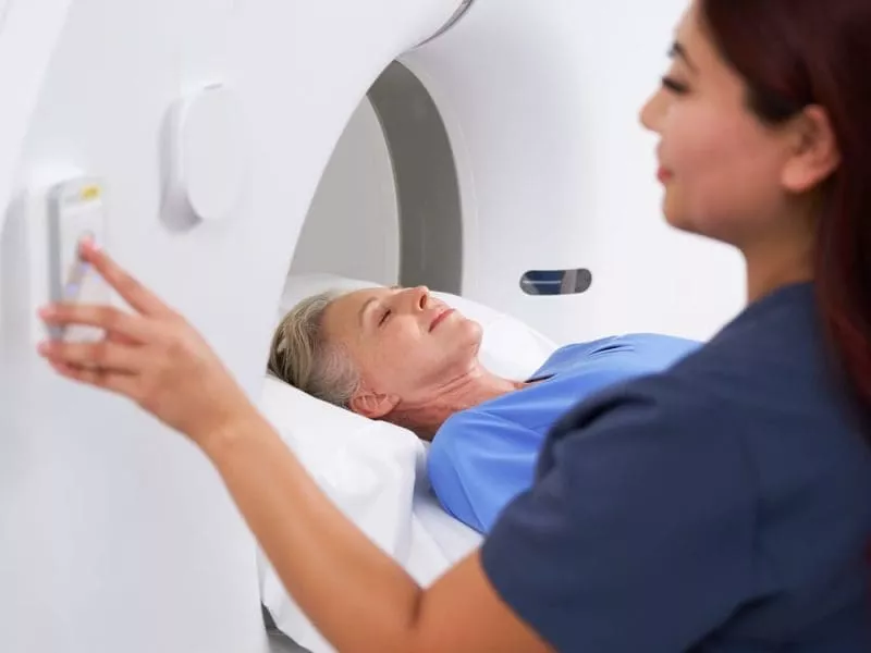 Radiographer adjusting MRI scanner controls as a patient lies inside the machine.