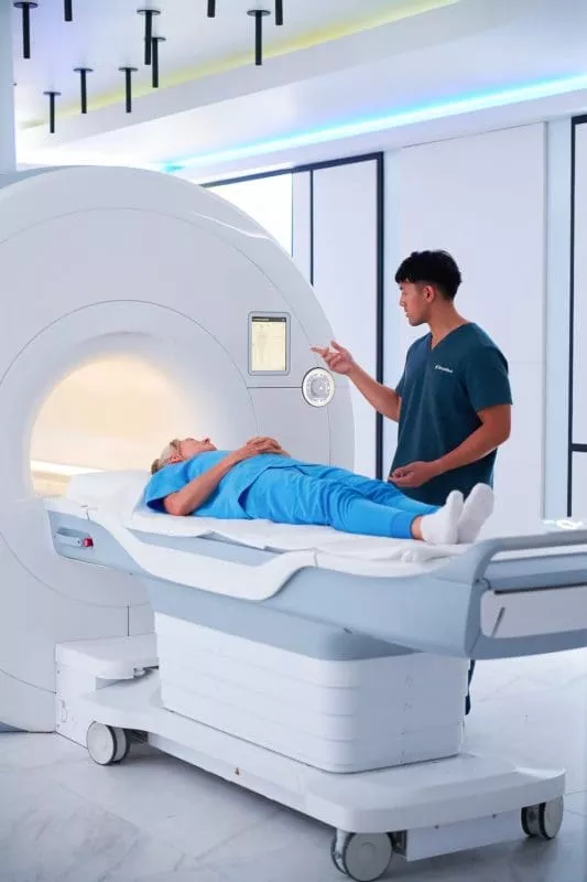 Clinician explains an MRI procedure to a patient lying on the scan table in front of the MRI machine.