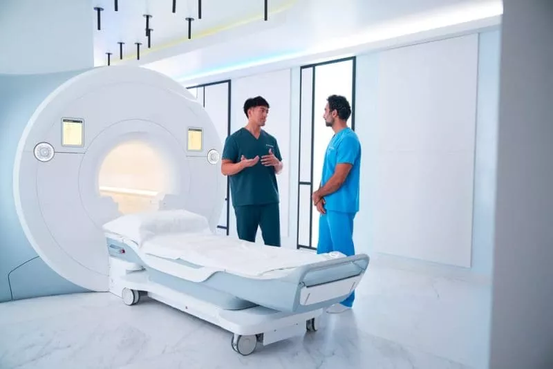 Two clinicians talking beside an MRI scanner in a bright, modern imaging room.