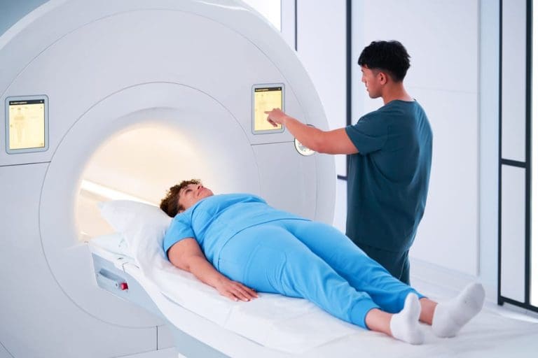 Patient lying on an MRI scanner bed while a clinician adjusts settings on the machine’s touchscreen.