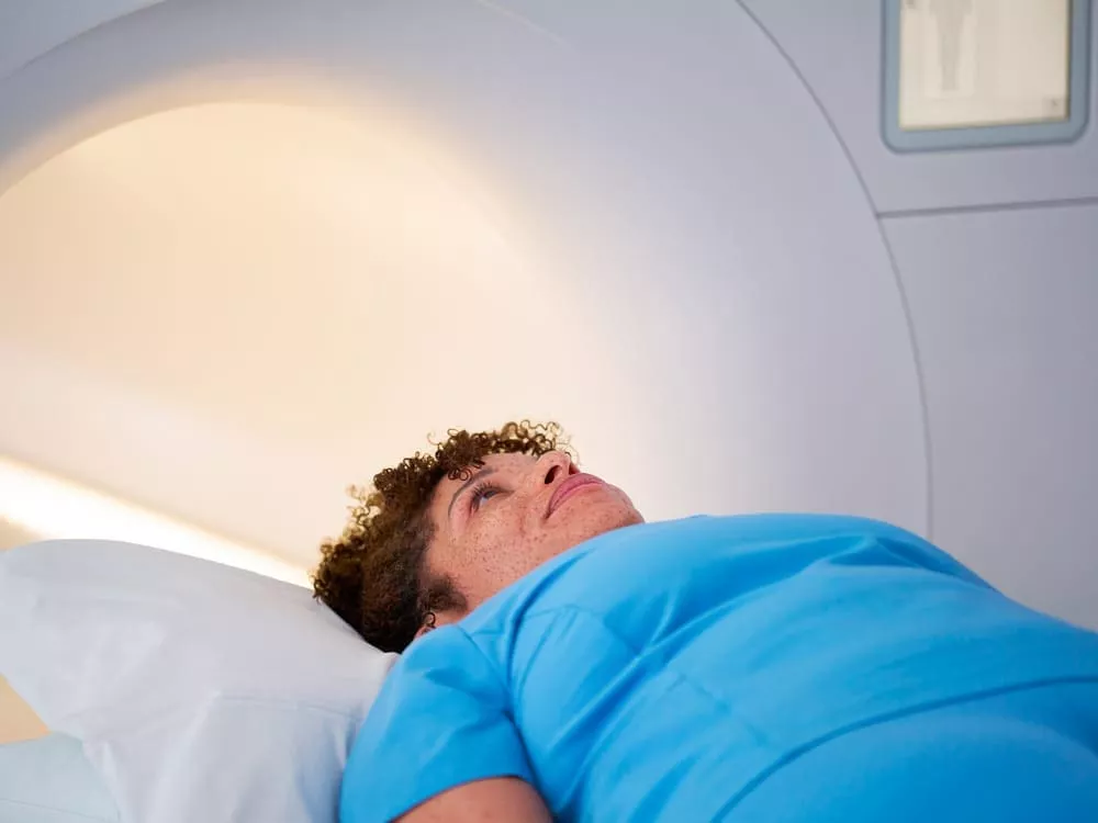 Patient lying on an MRI scanner bed, looking upward with head supported by a pillow.