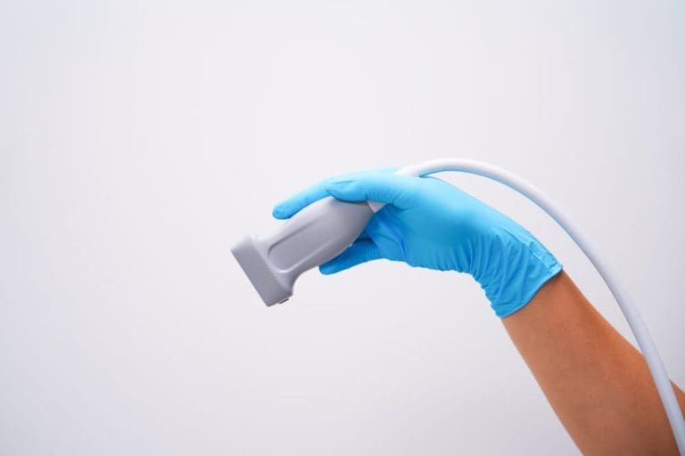 Gloved hand holding an ultrasound transducer against a clean white background.